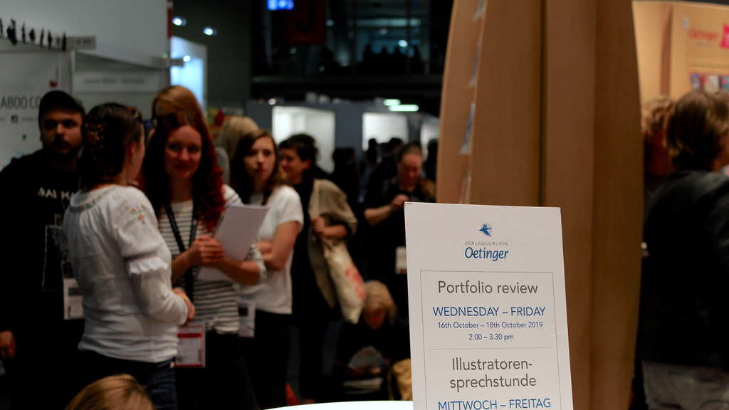 Menschen in einer Warteschlange. Vor ihnen scharf ein Hinweis mit der Aufschrift Illustratoren-Sprechstunde